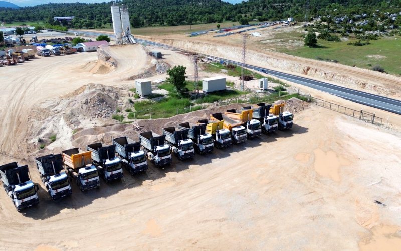Silifke–Gülnar yolu şantiyesinde sıralanmış damperli kamyon filosu ve yol kesimi